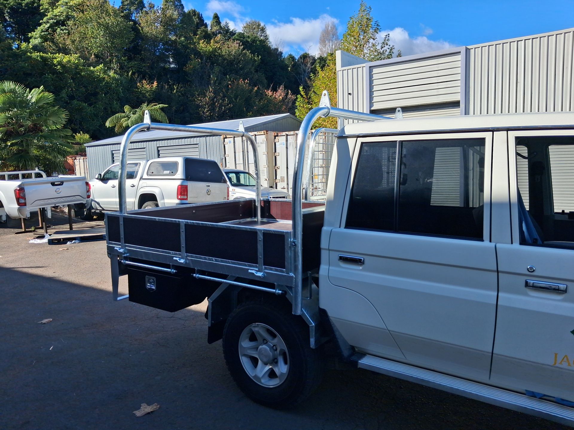 White flatbed pickup truck parked in a lot, rear view with wooden side rails and crane frame.
