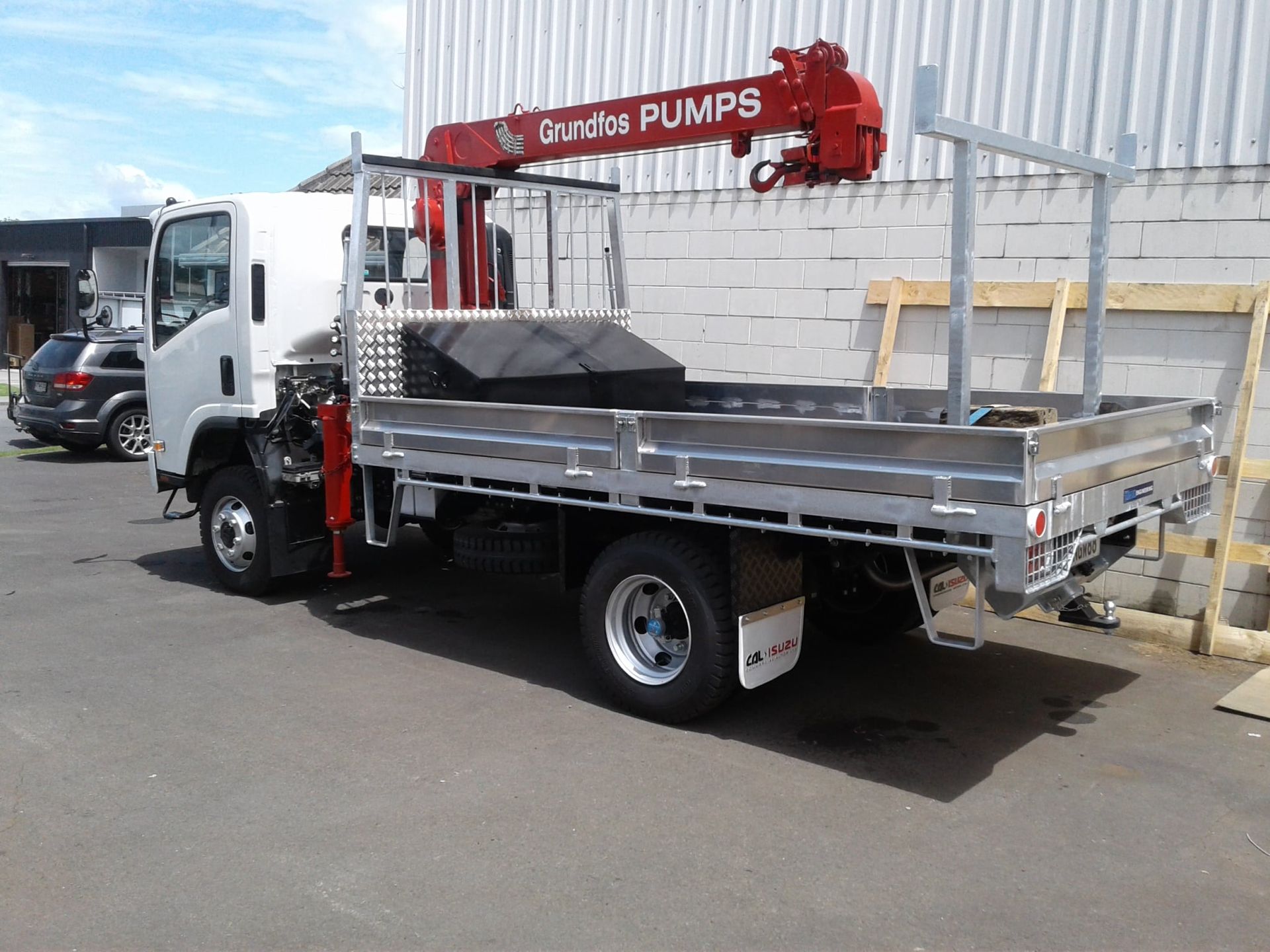 Flatbed truck parked on a wet lot beside a white building, carrying a large wooden crate.