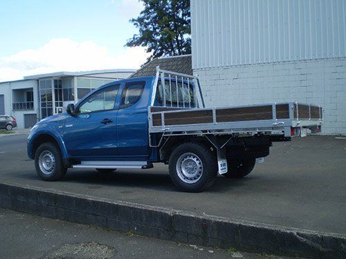 Blue pickup truck parked by a curb beside a white building