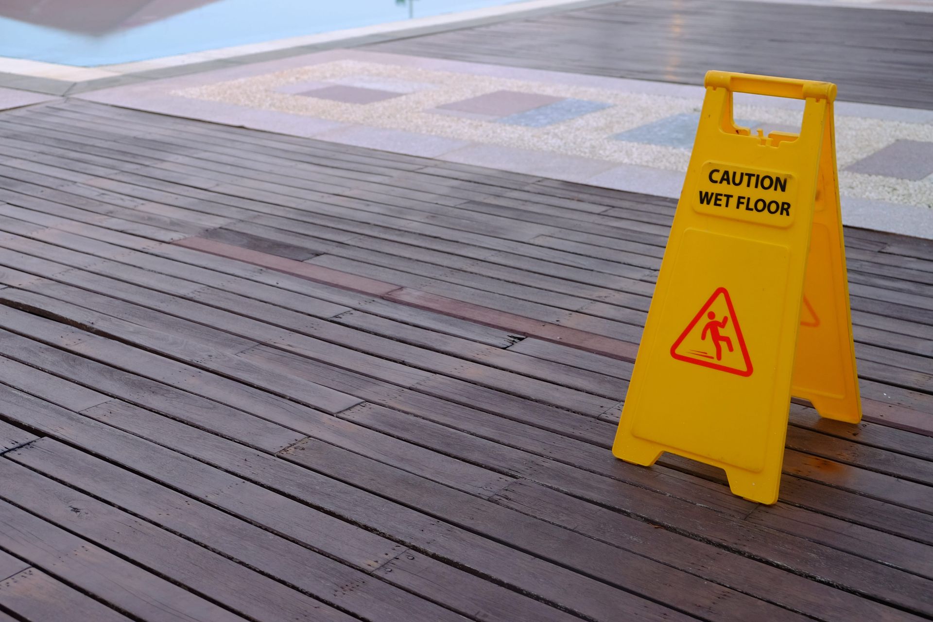 Yellow “Caution Wet Floor” sign on a wooden deck near a pool.