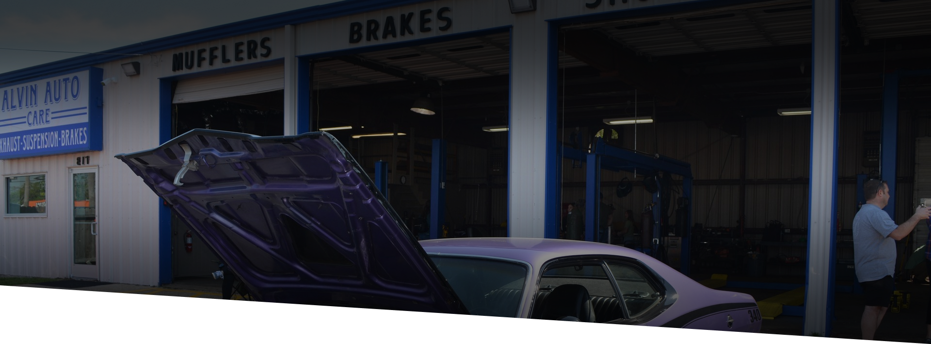 A purple car with a raised hood sits in front of a car repair shop with the words 