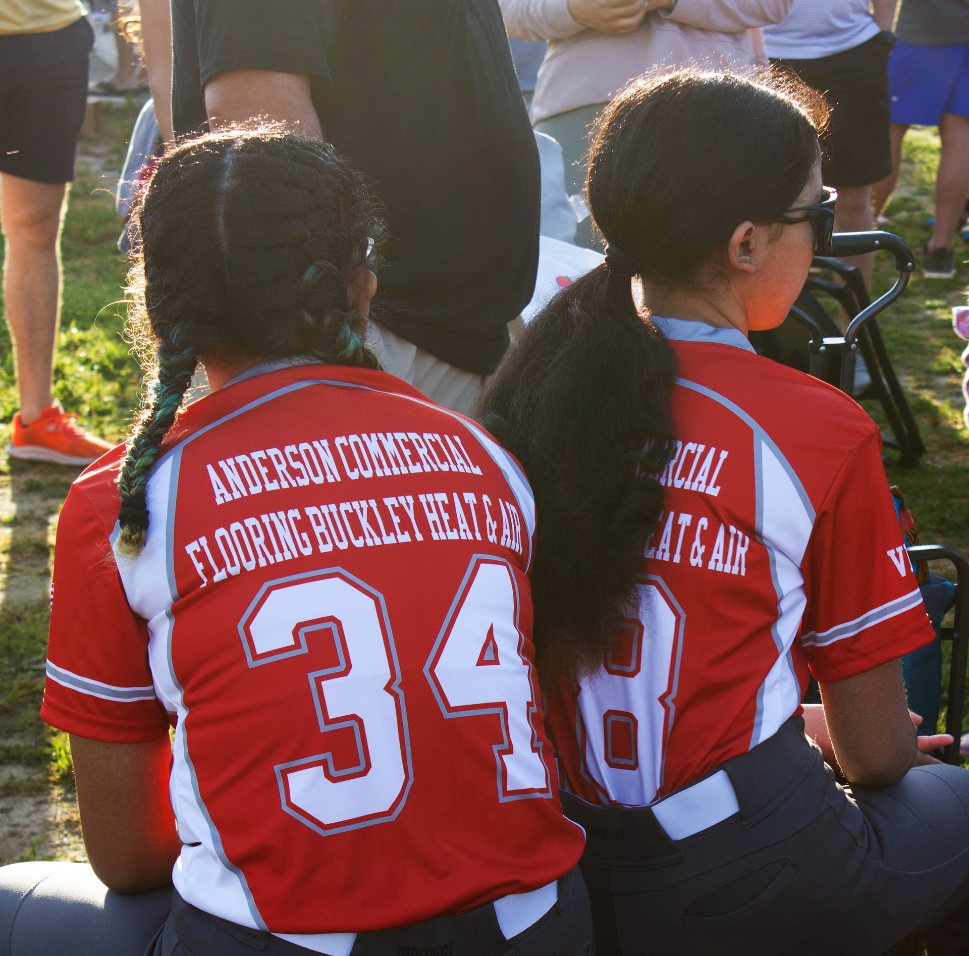 Softball players in red jerseys displaying the name of their business sponsor