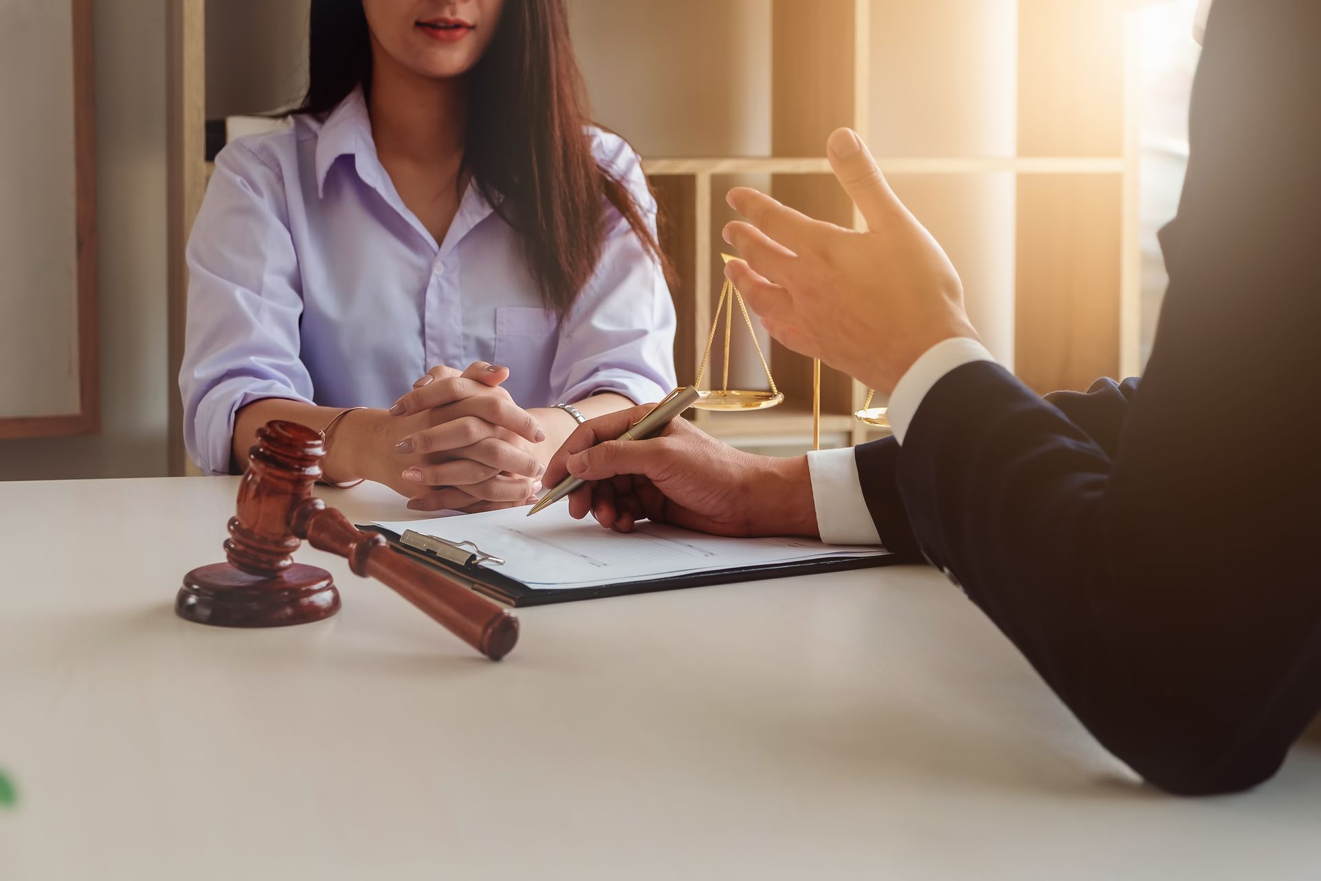 A partial view of a lawyer explaining a document to his client with a gavel on the desk.