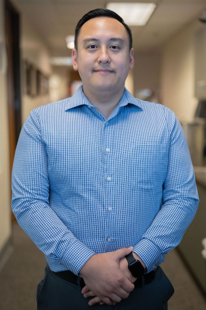 Man in a blue checkered shirt standing in a hallway with hands clasped