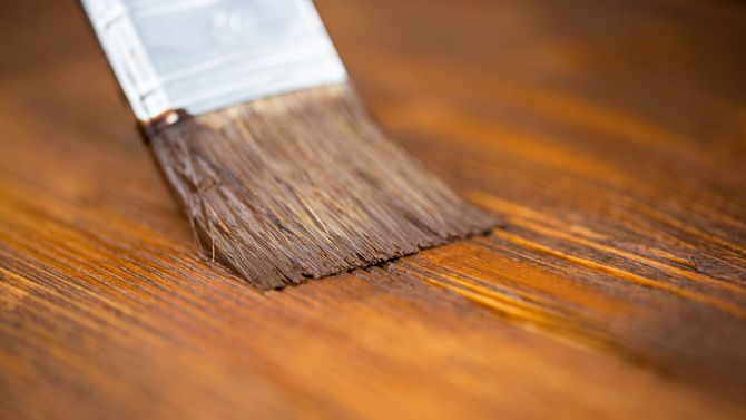 Paintbrush applying brown varnish to a wooden surface