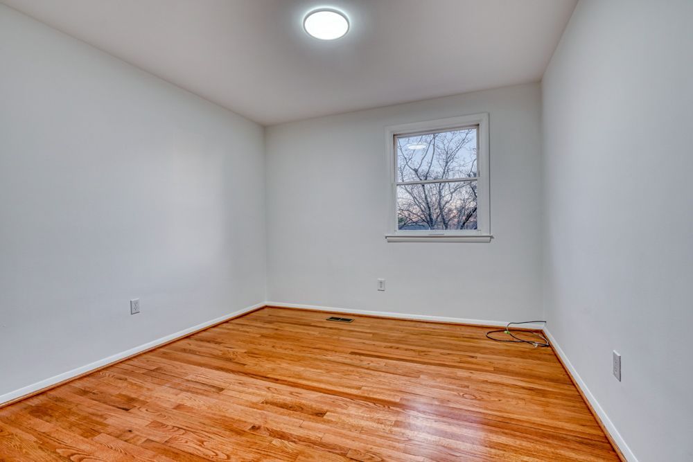 An empty bedroom with hardwood floors and white walls.