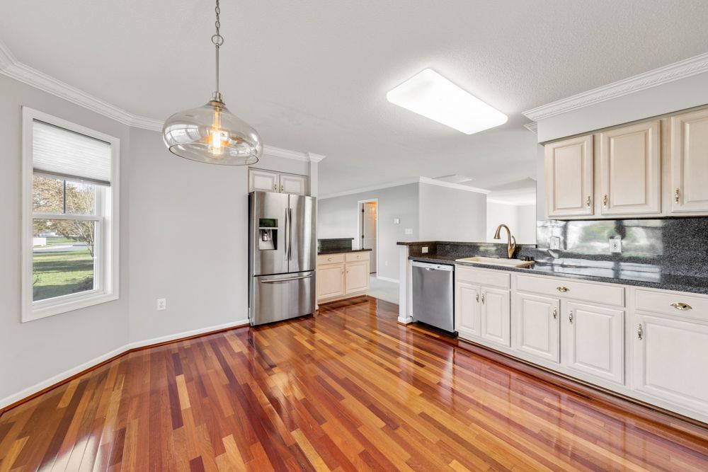 A kitchen with hardwood floors , white cabinets , stainless steel appliances and a refrigerator.