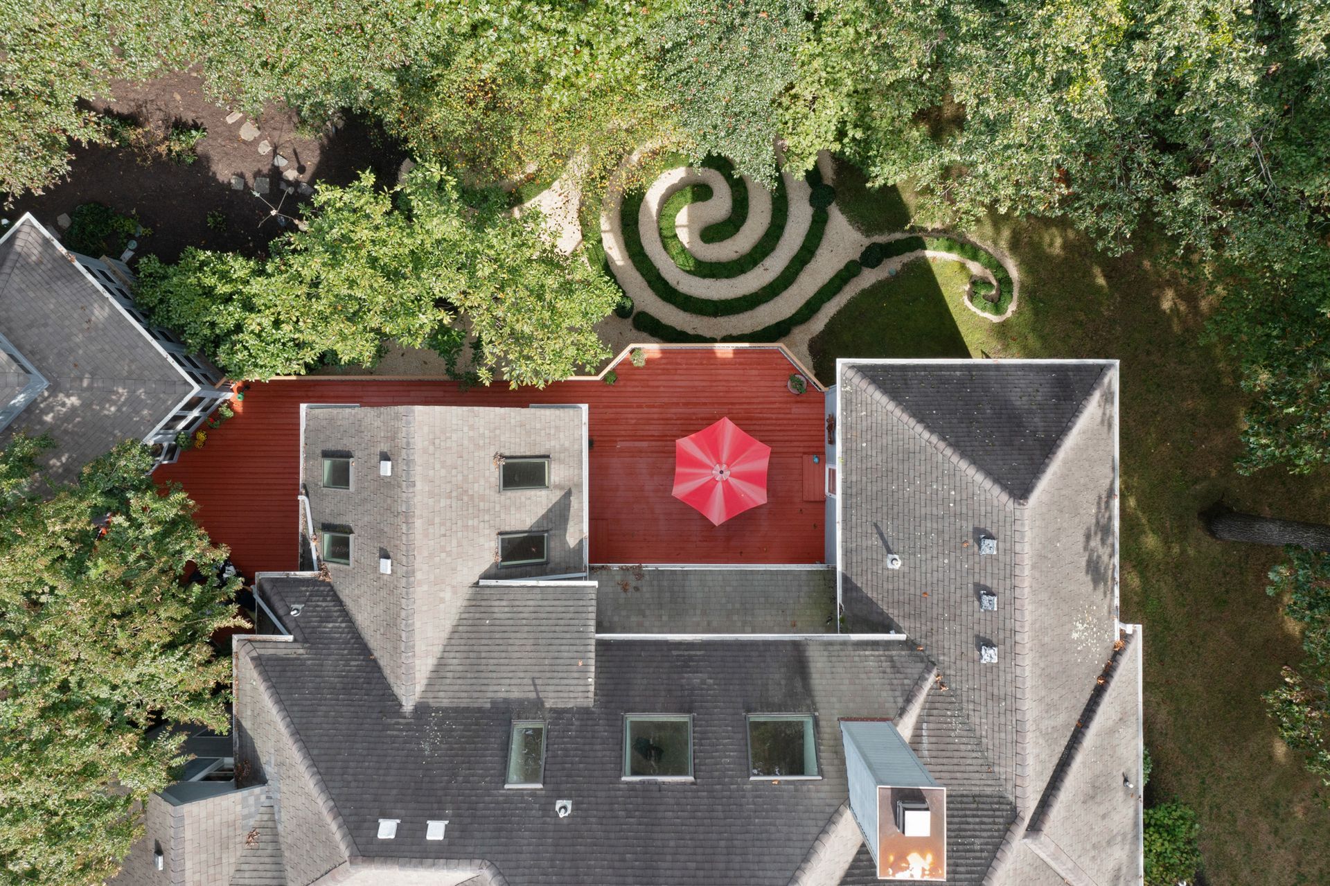 An aerial view of a house with a red umbrella on the roof and beautiful spiral lawn. Aerial drone shoot by Craig Westerman.
