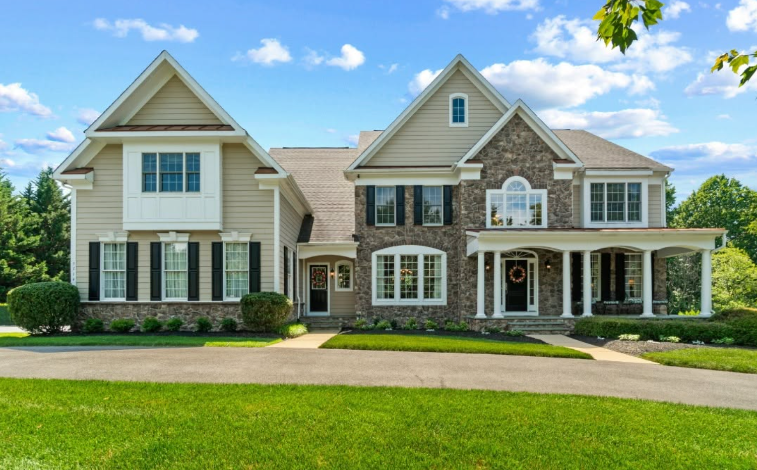 Suburban home with stone and siding exterior, manicured lawn, and landscaping at curb side view.