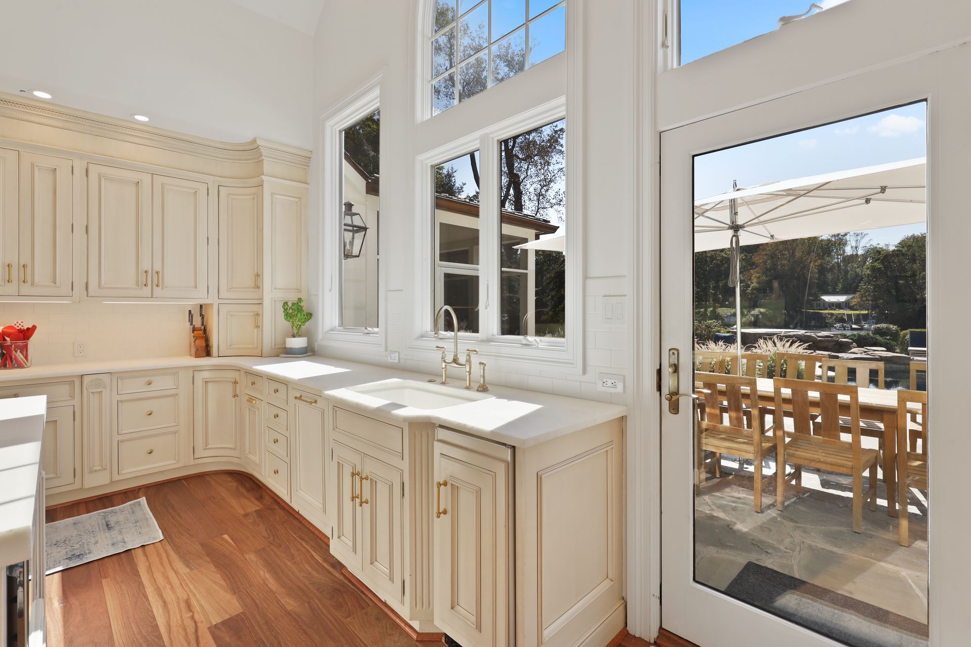 A kitchen with white cabinets and hardwood floors and a large window.