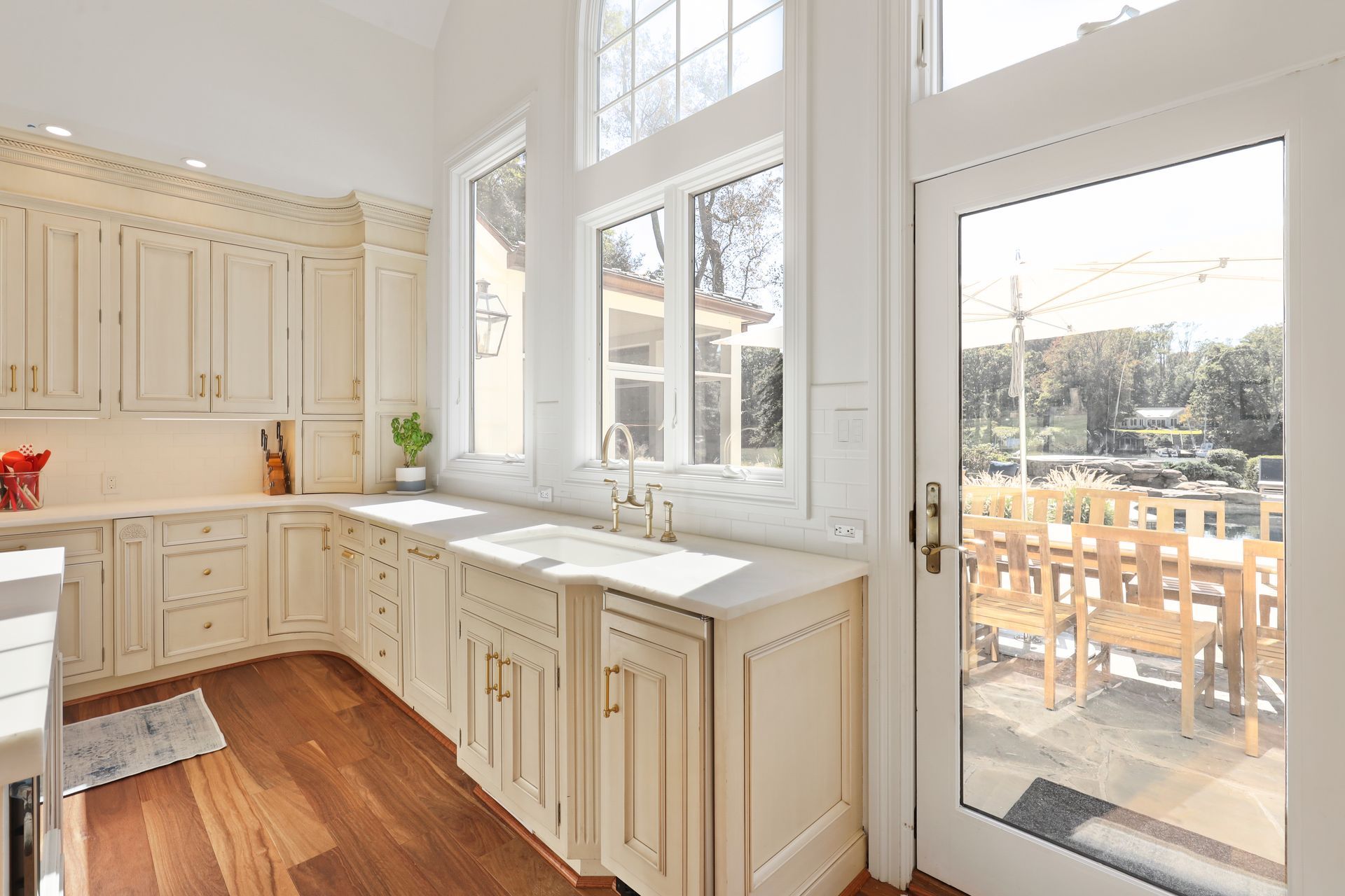 A kitchen with white cabinets and hardwood floors and a large window.