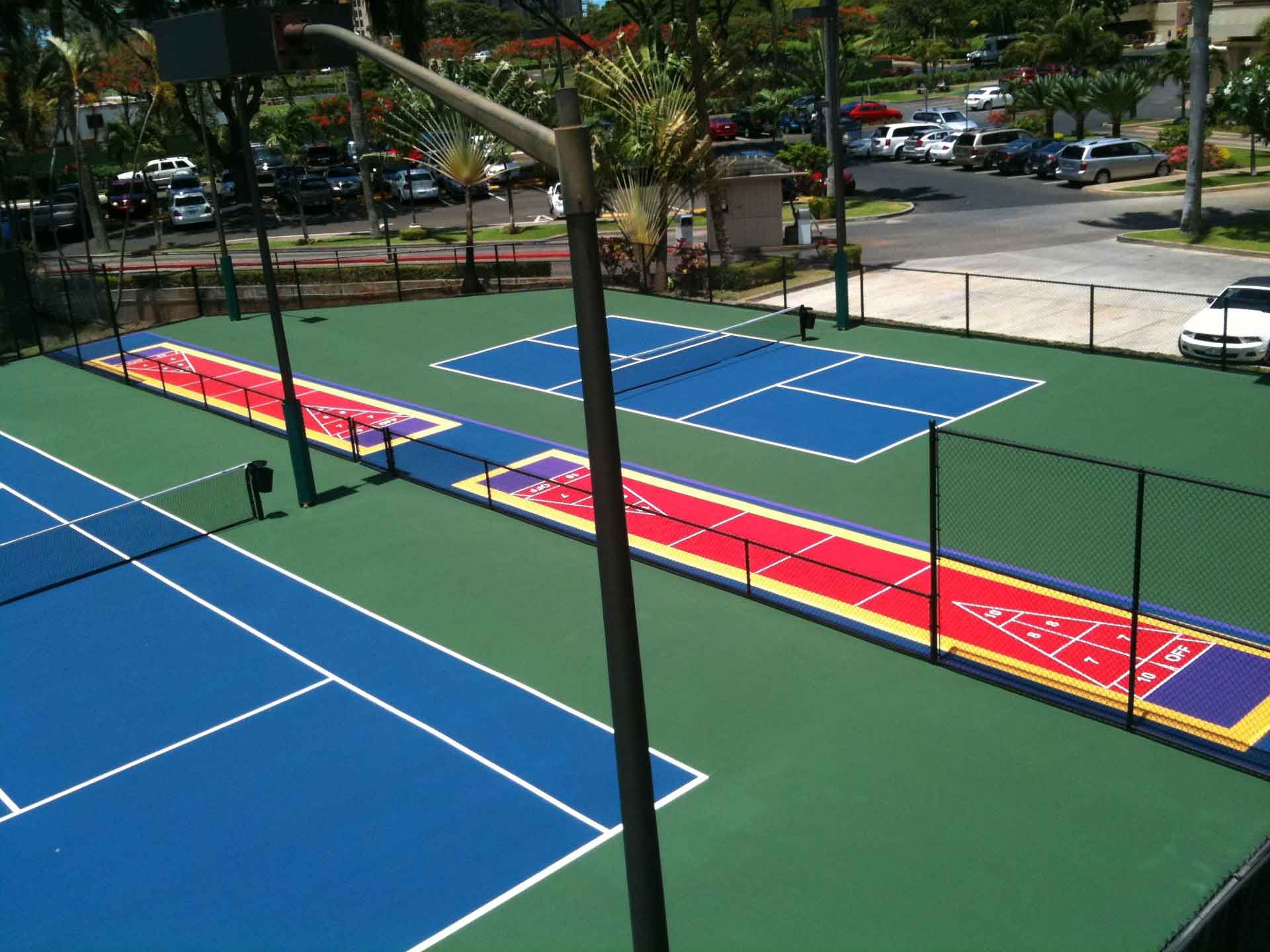 Overhead view of a sports court with blue and green surfaces, including tennis courts, pickleball courts, and shuffleboard.