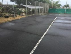 Tennis court with a cracked surface and a wire enclosure.