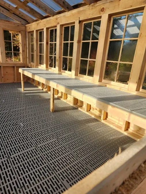 A row of wooden benches in a room with lots of windows.