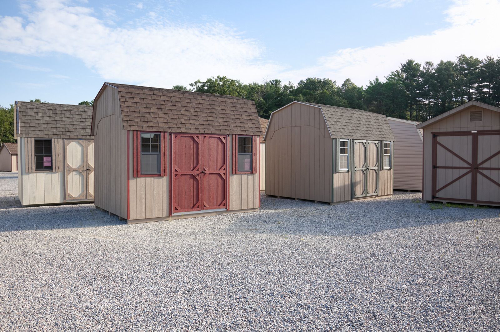 A group of sheds are lined up in a gravel lot.