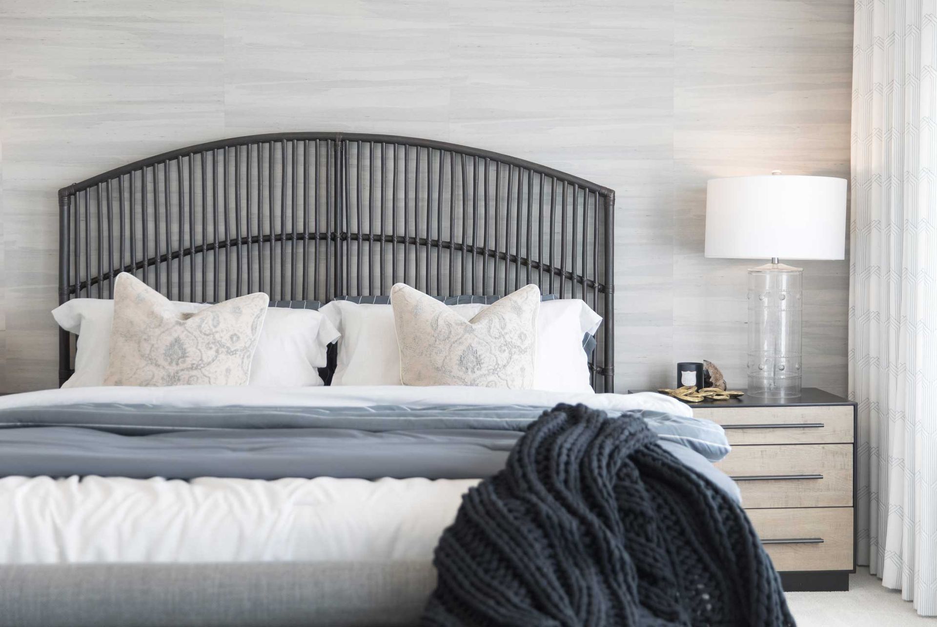 A bedroom with a bed , nightstand , lamp and a wicker headboard.