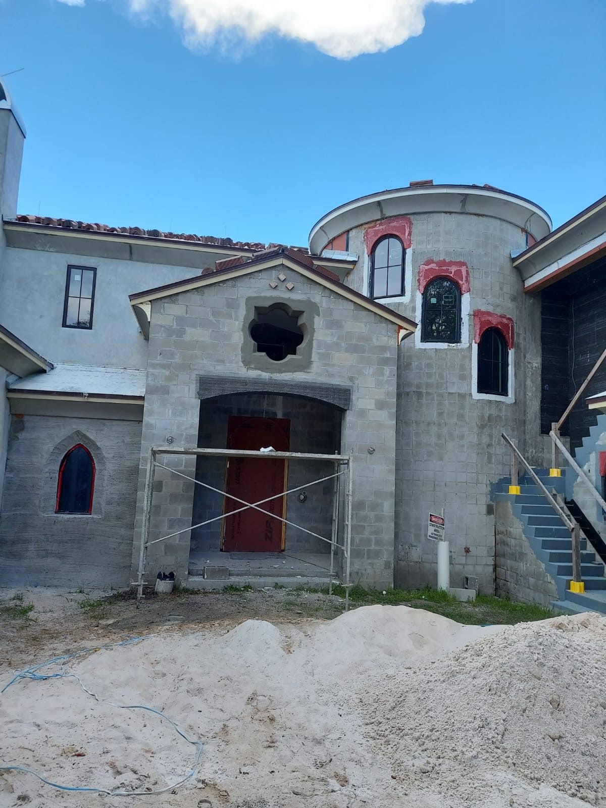 Gray castle-like building under construction with a red door and windows, a blue sky in the background.