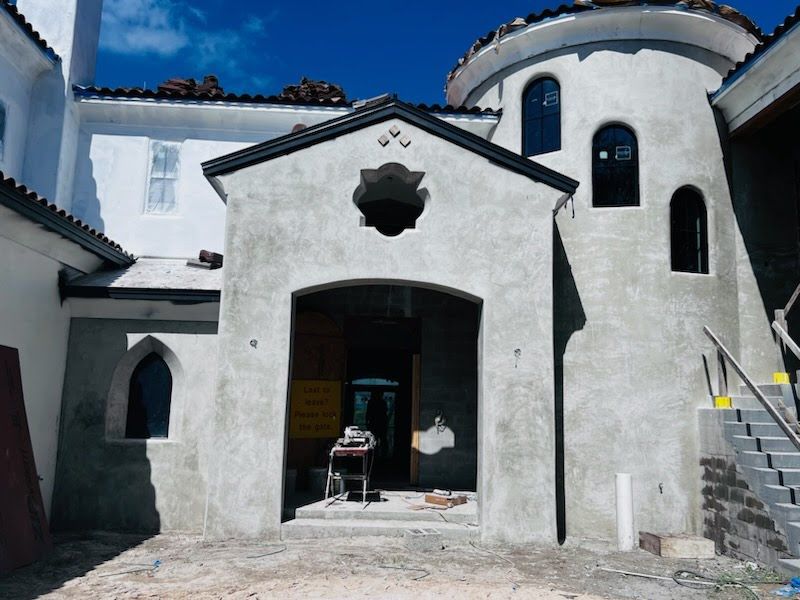 Exterior of a light grey castle-like building under construction.  A door and turret are visible.