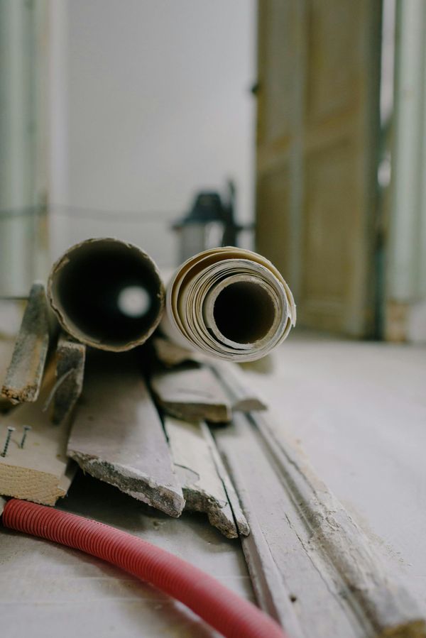 Close-up view of two cardboard tubes resting on construction debris and a red hose on a floor.