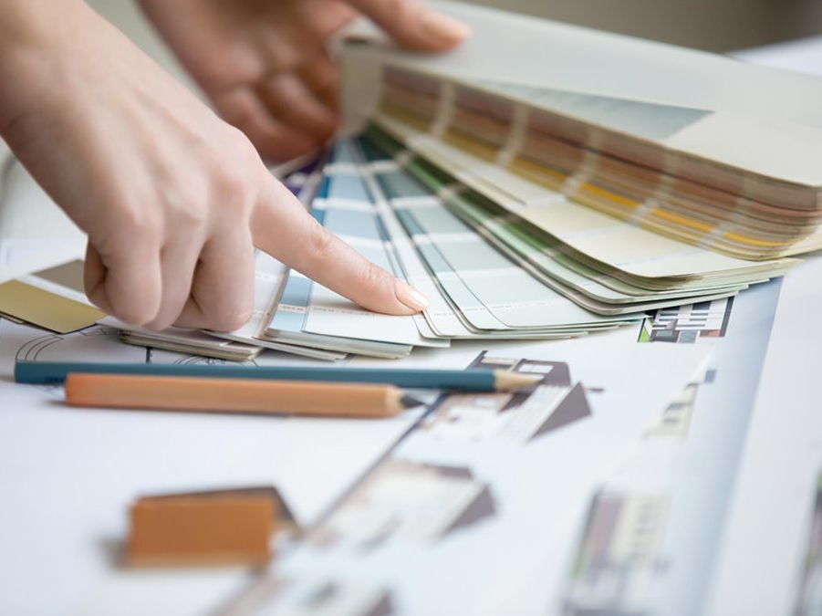 Hands pointing at paint swatches on top of architectural plans. Pencils are nearby.