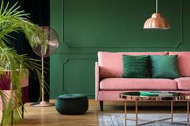 Living room with pink sofa, green wall, copper accents, and potted plant.
