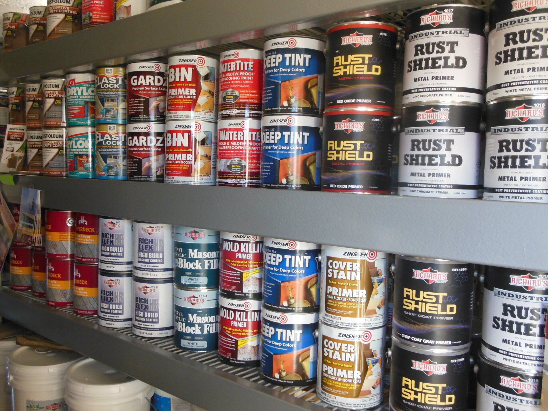 Paint cans on shelves, various brands and colors, in a hardware store setting.