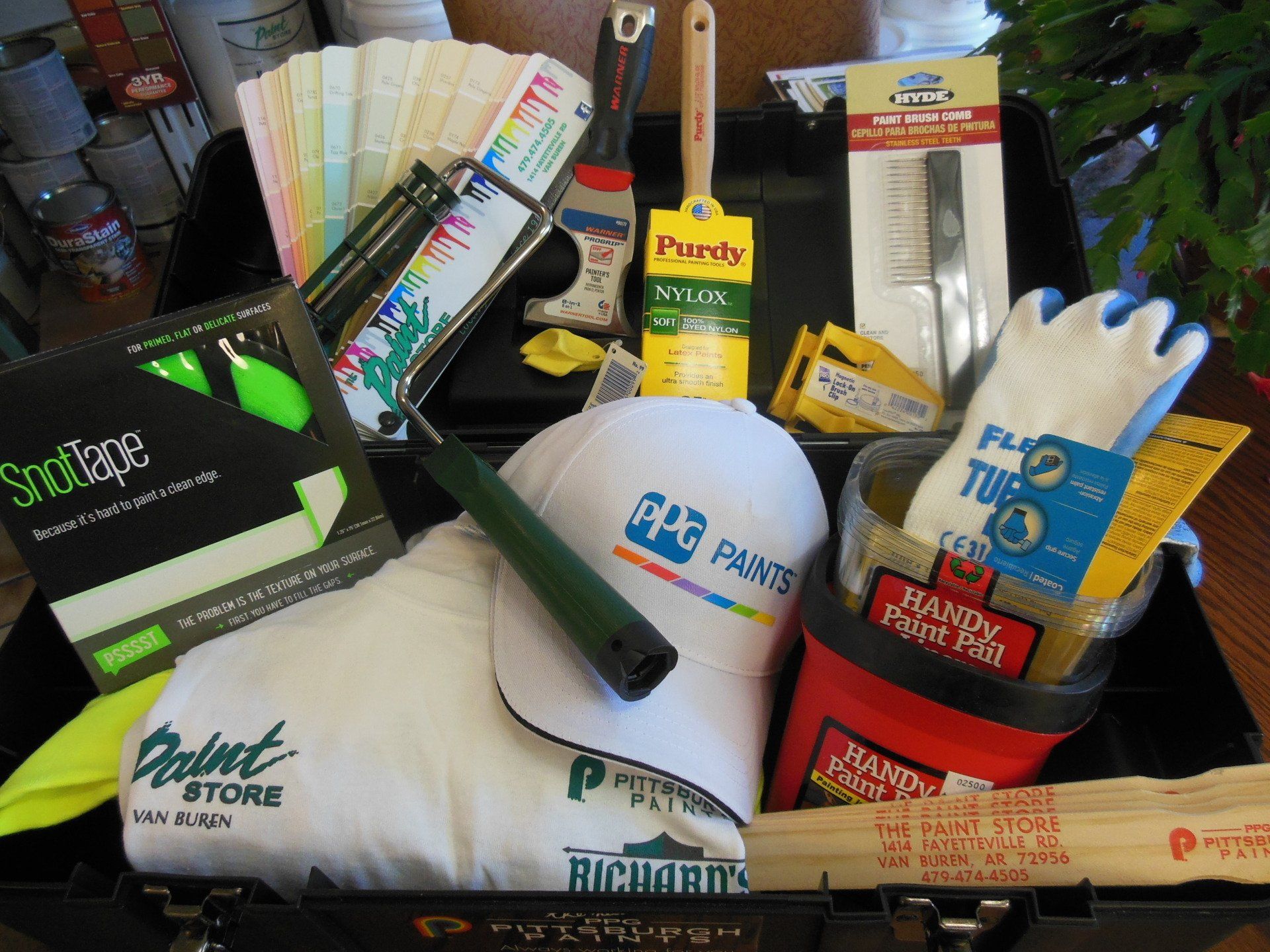 Paint supplies in a black toolbox, including brushes, roller, tape, gloves, and color swatches.