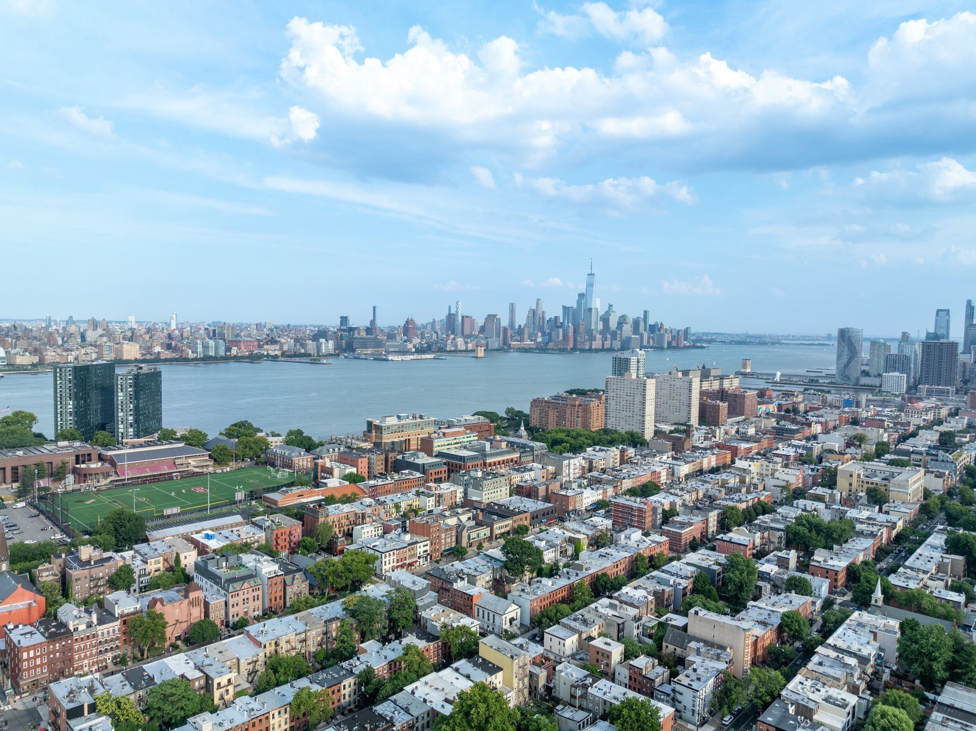 Cityscape with river, buildings, and a skyline under a cloudy blue sky.