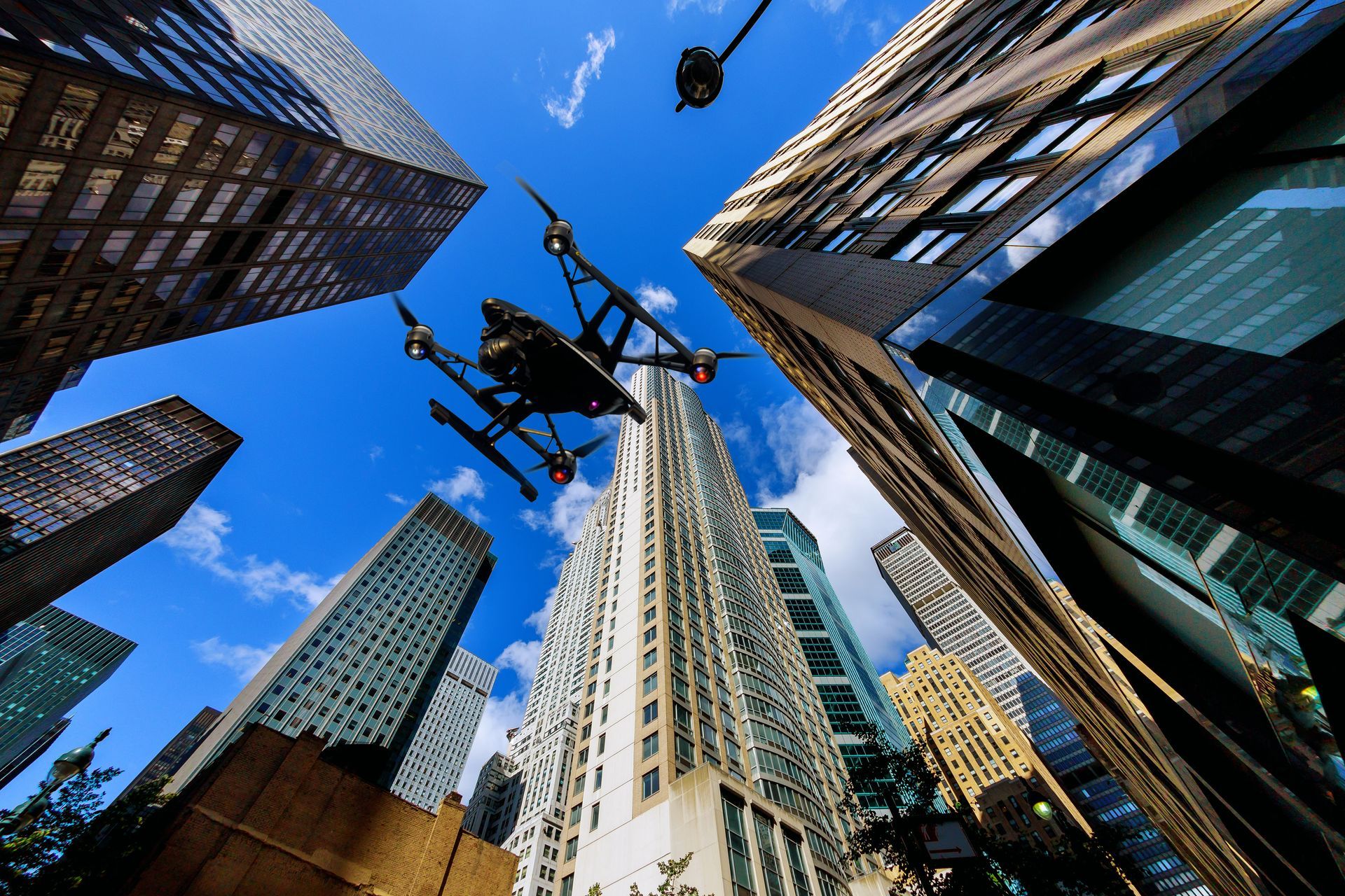 Drone flying between skyscrapers against a blue sky.