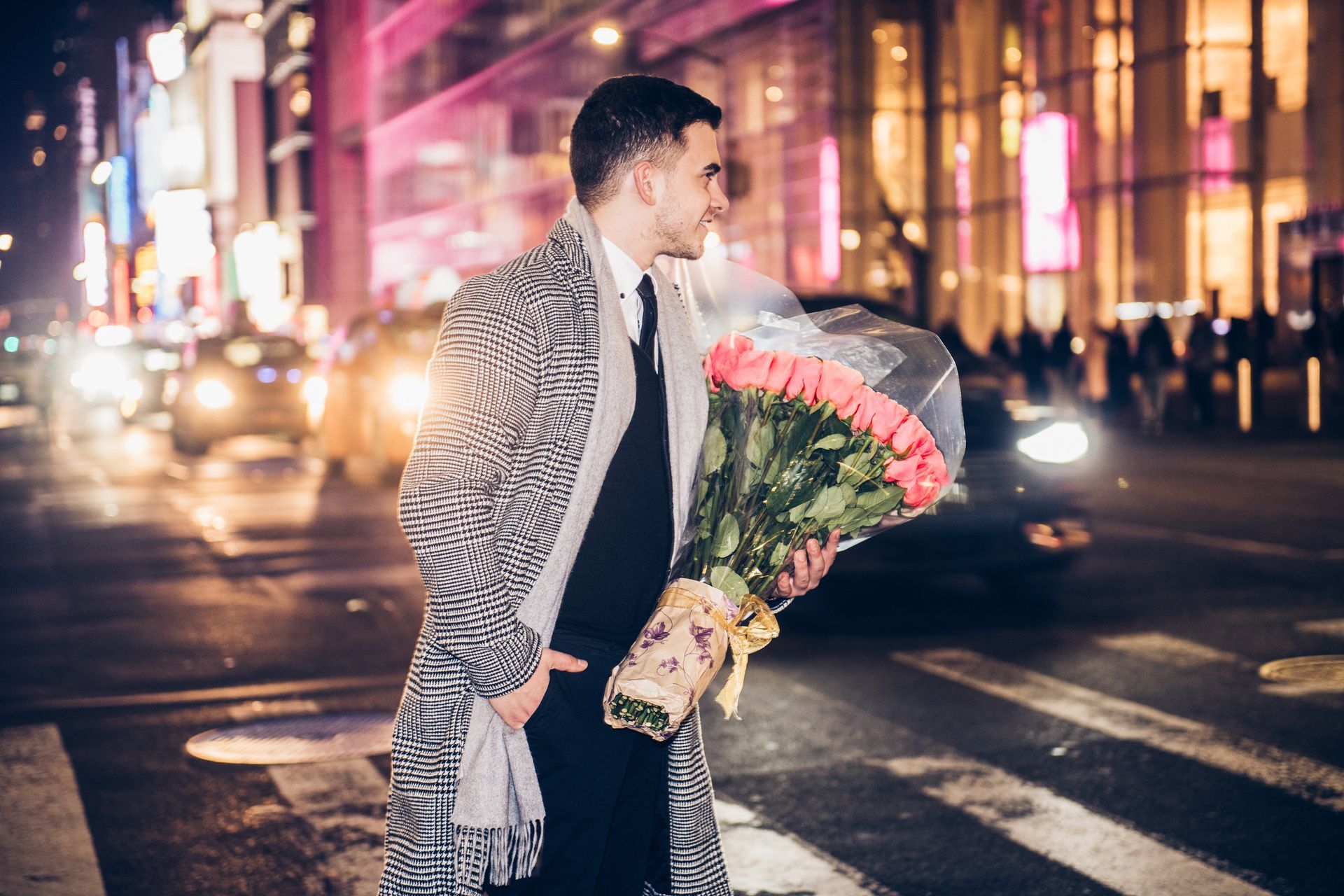 Man holding roses on a city street at night, looking back over his shoulder.