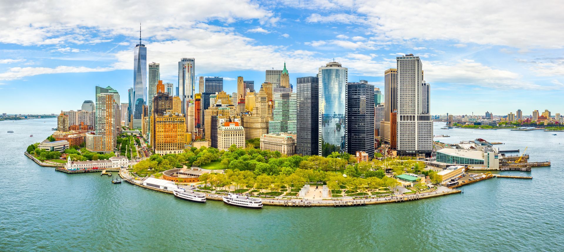 New York City skyline with blue water and sky. Skyscrapers and green park are visible.