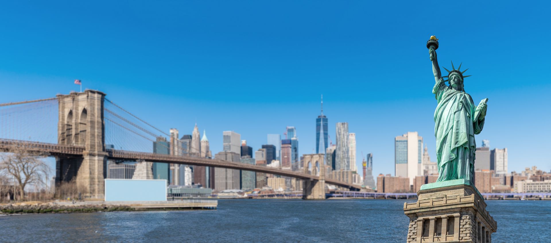 There is a statue of liberty in the foreground and a bridge in the background.