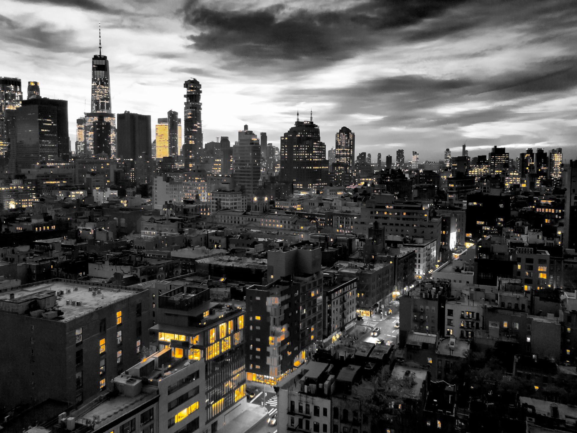 City skyline at dusk, mostly black and white with illuminated buildings, including one with gold.