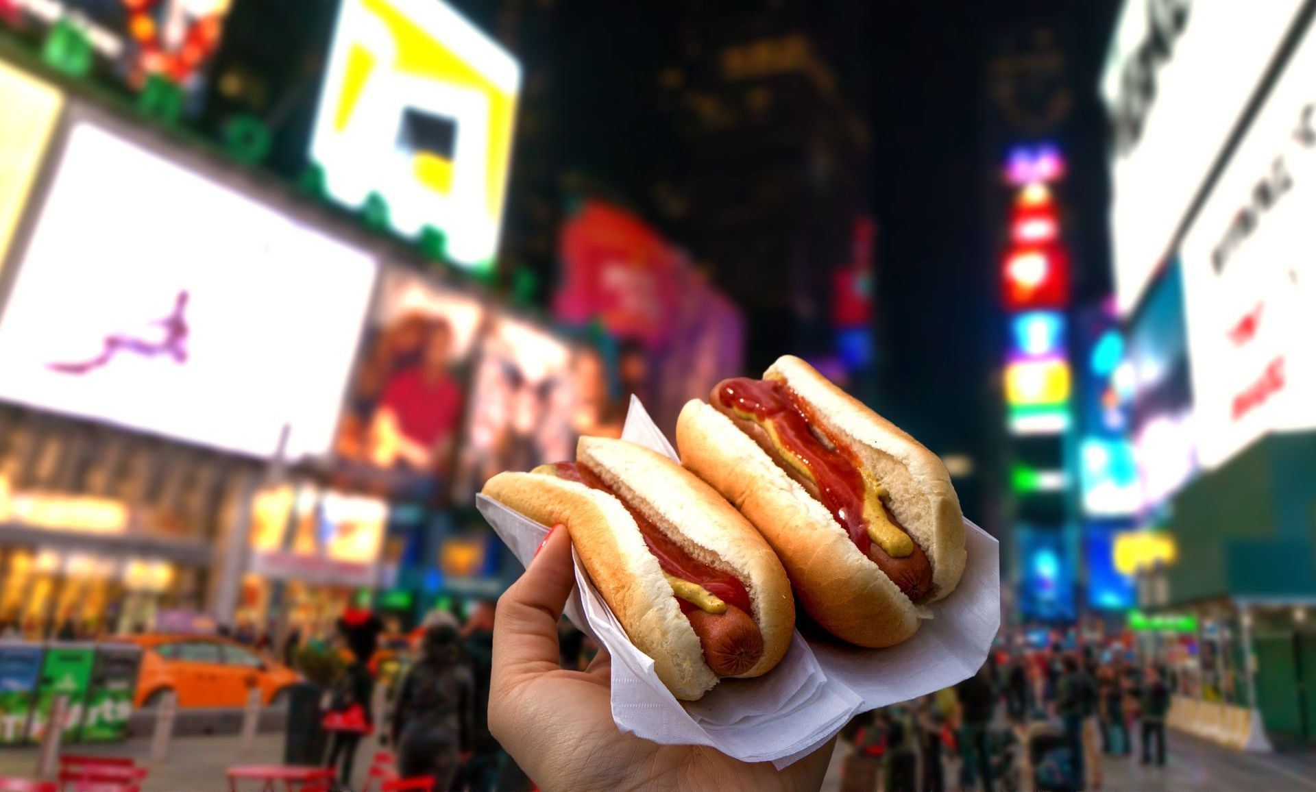 A person is holding two hot dogs in front of a crowd of people.