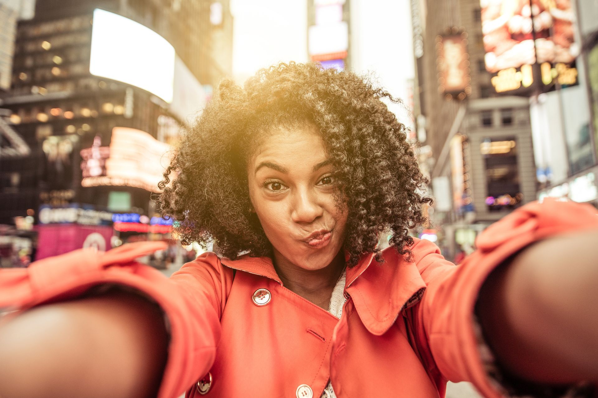 Woman taking a selfie, making a face, in Times Square. She's wearing an orange coat.