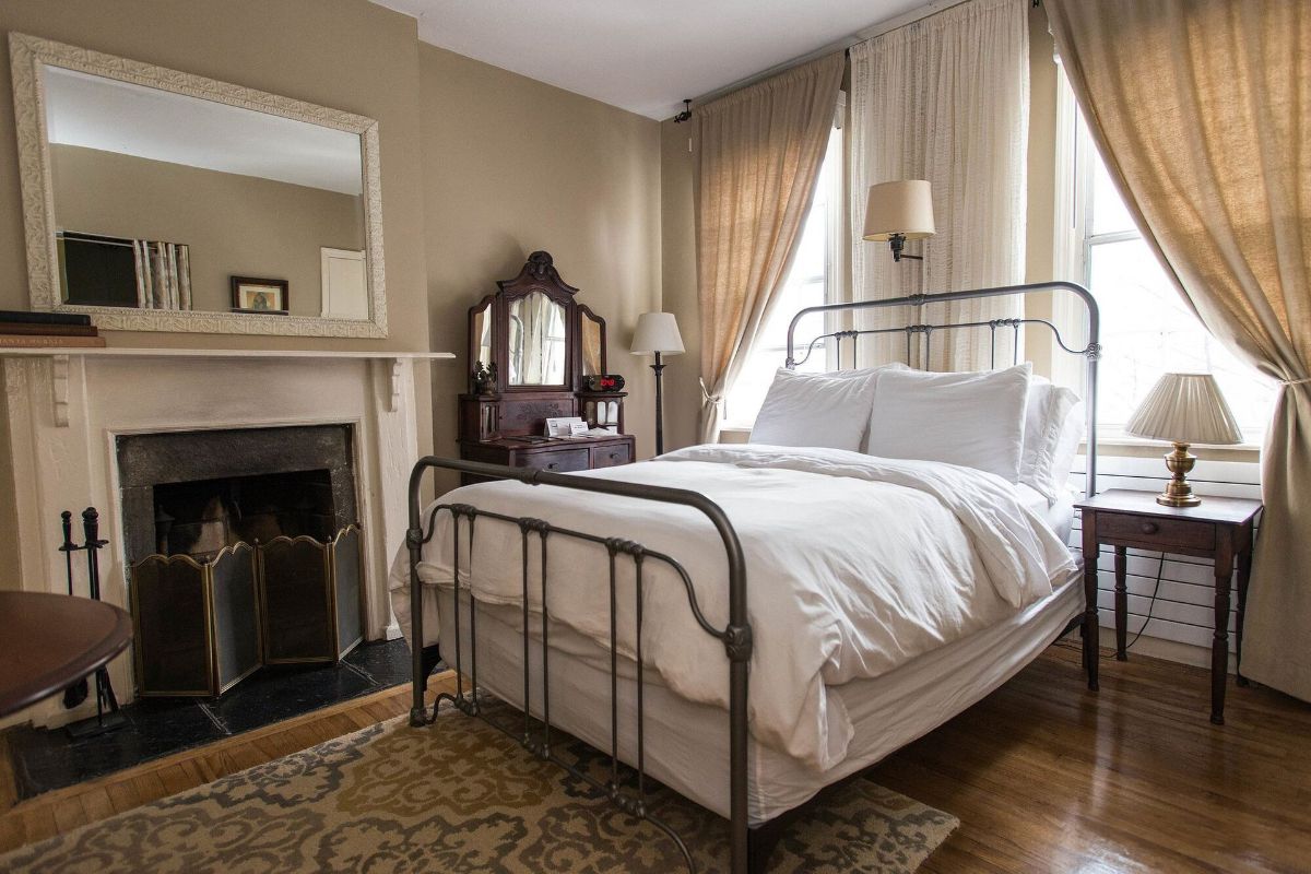 a bedroom with a bed , fireplace , mirror and nightstand .