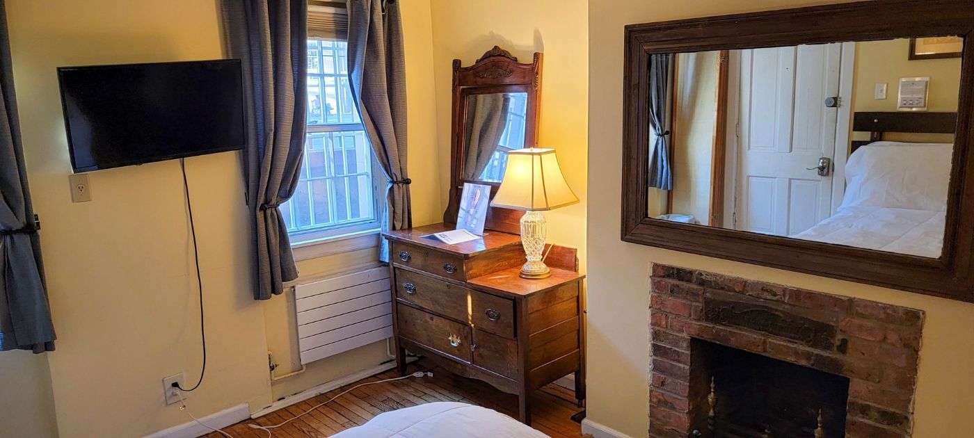 a bedroom with a bed , dresser , mirror and fireplace .
