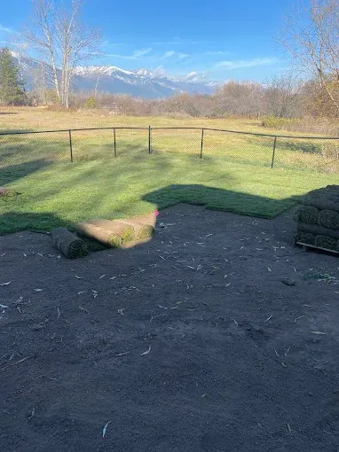 A partially sodded lawn in front of a wire fence and field with snow-capped mountains in the distance.