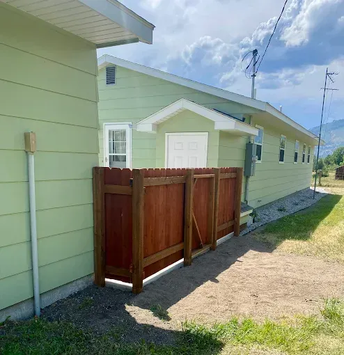 A light green house with a small white door and a new, dark wood privacy fence in the yard.