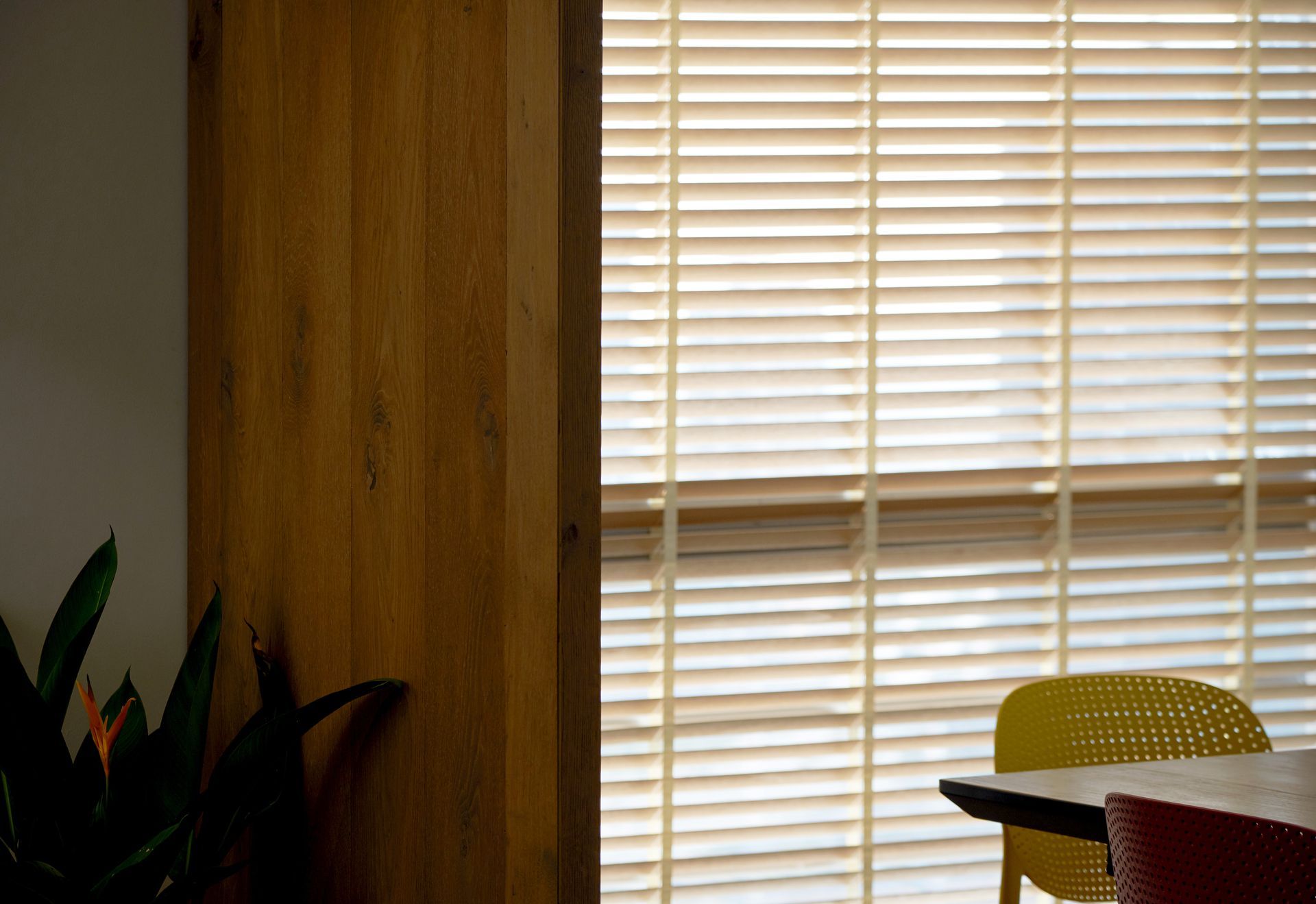 Indoor room with wooden wall, white blinds, and yellow and red chairs by a table