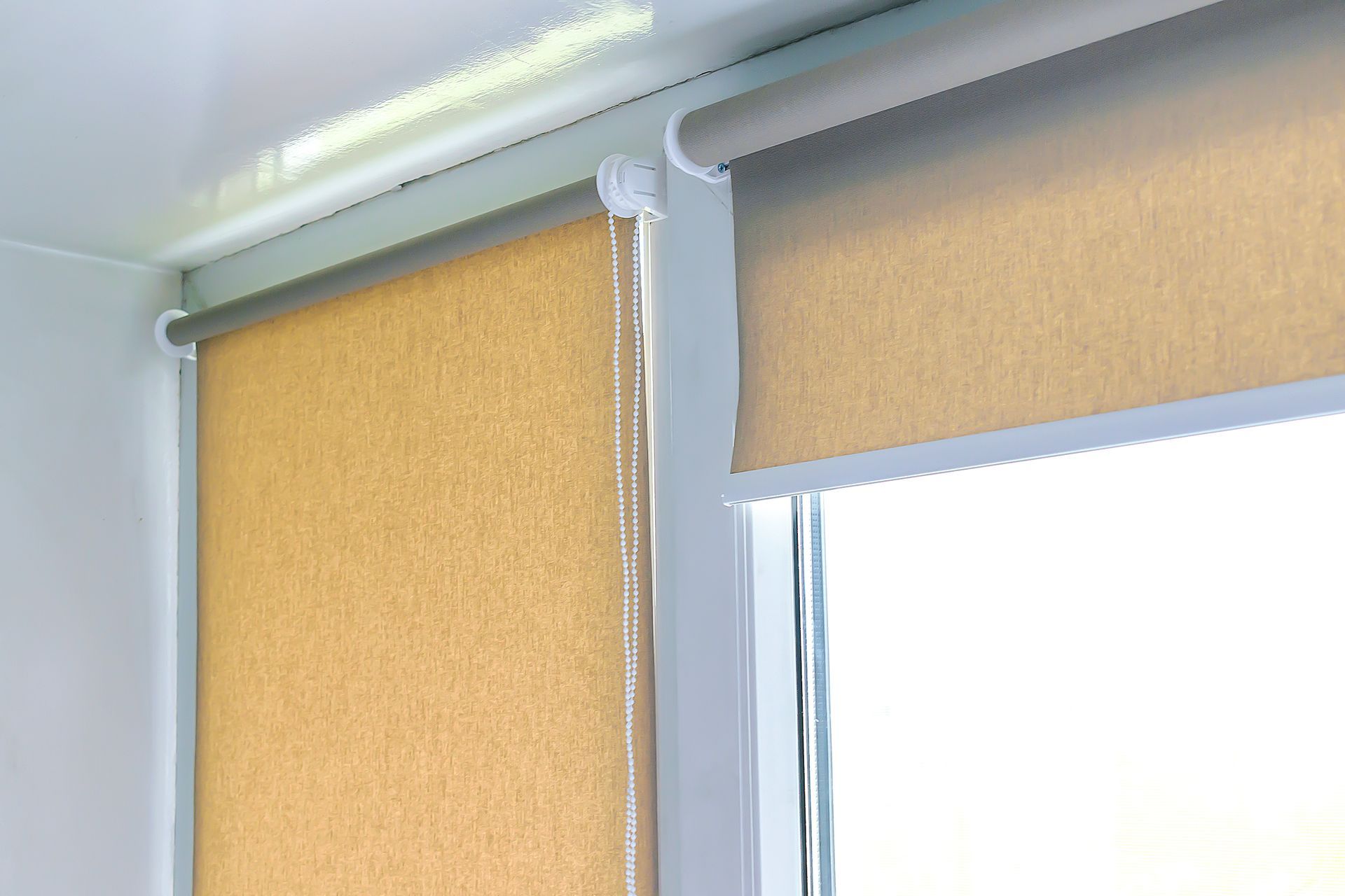 Close-up of two windows with beige roller blinds and white frames in a bright room