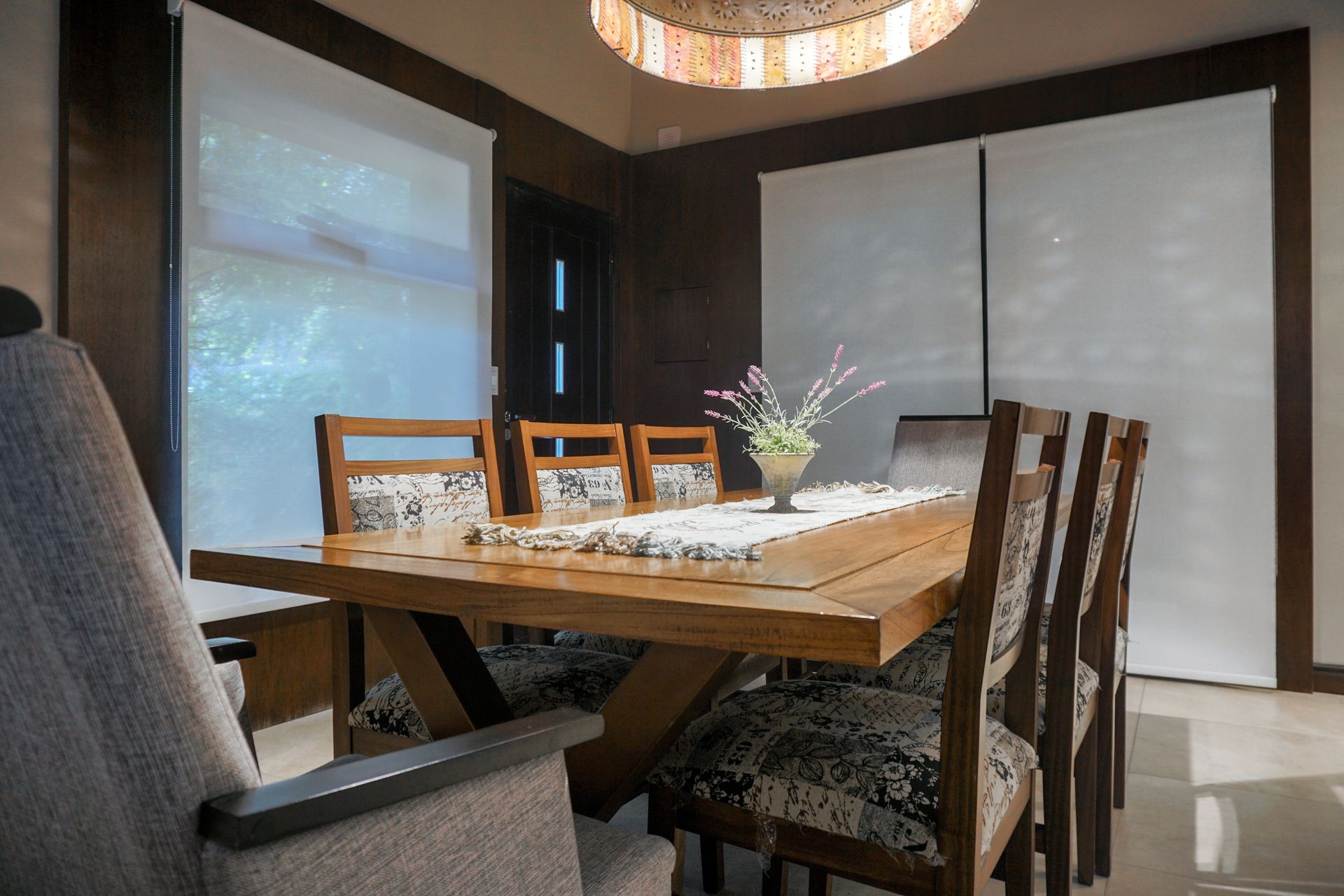 Modern dining room with a wooden table, upholstered chairs, and large windows with blinds