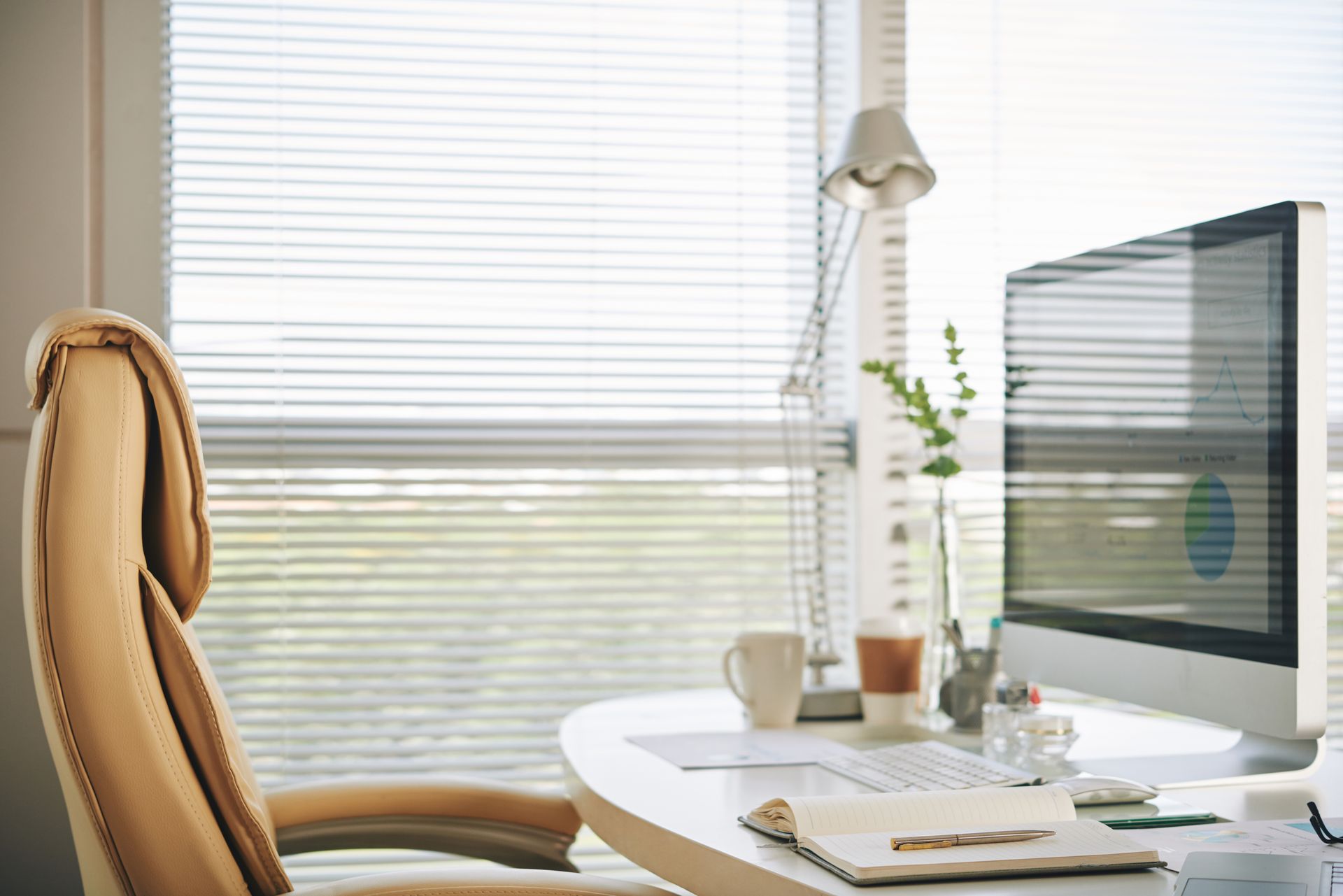 Bright home office desk with computer, chair, lamp, and window blinds