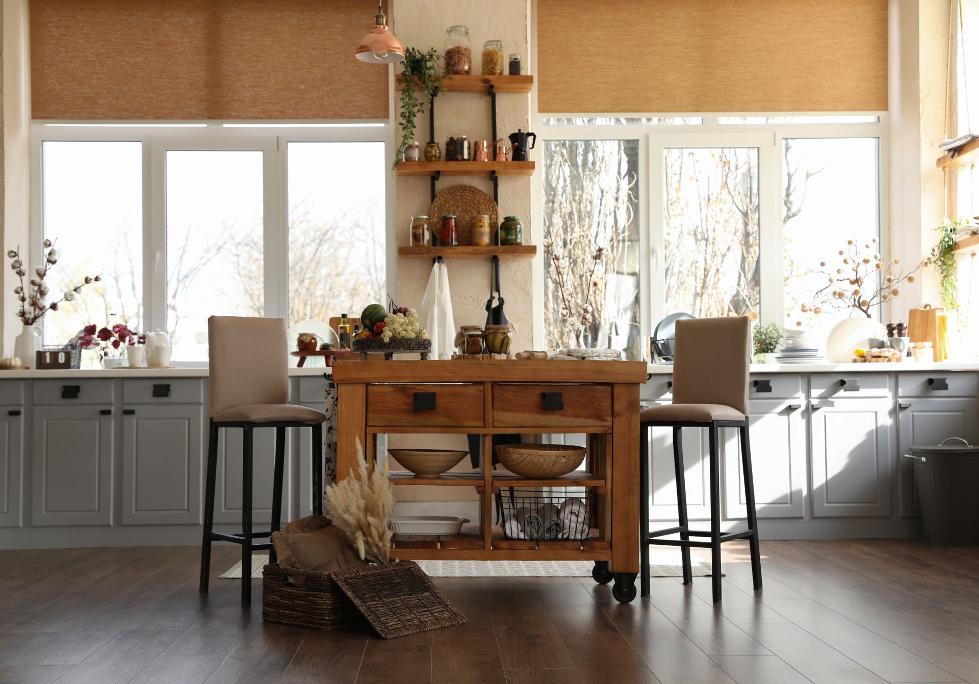 Bright kitchen with a wooden island, two stools, gray cabinets, and woven wood shades.