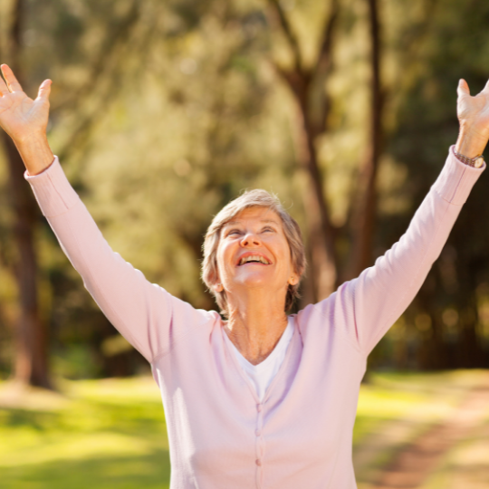An elderly woman with her arms outstretched in a park