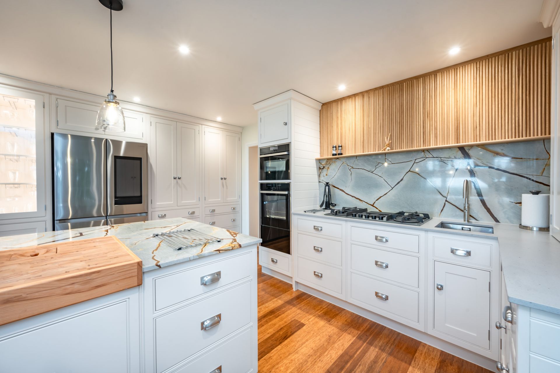 A kitchen with white cabinets , wooden floors , stainless steel appliances and a large island.