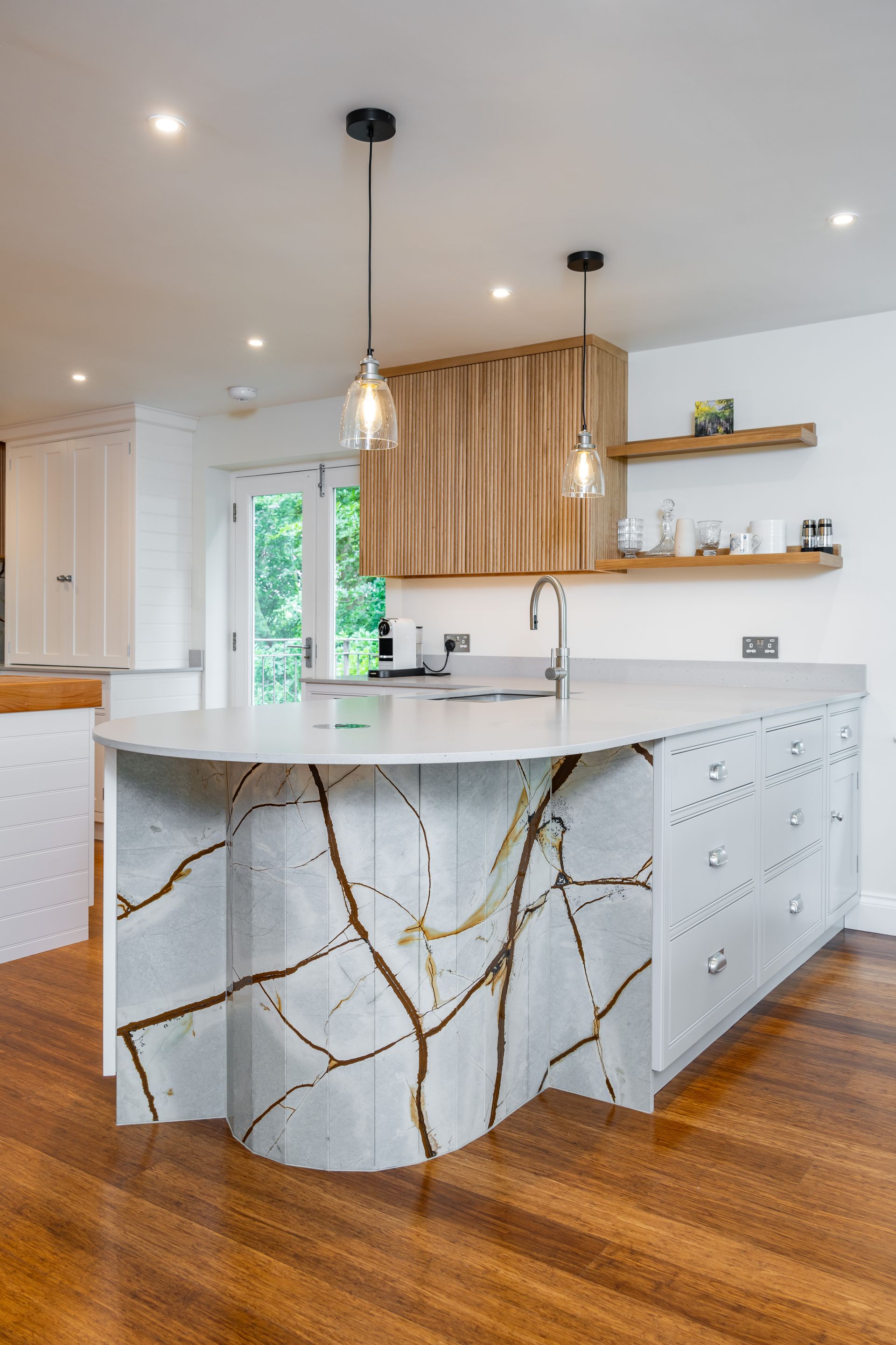 A kitchen with a large island , stools , a refrigerator and a sink.