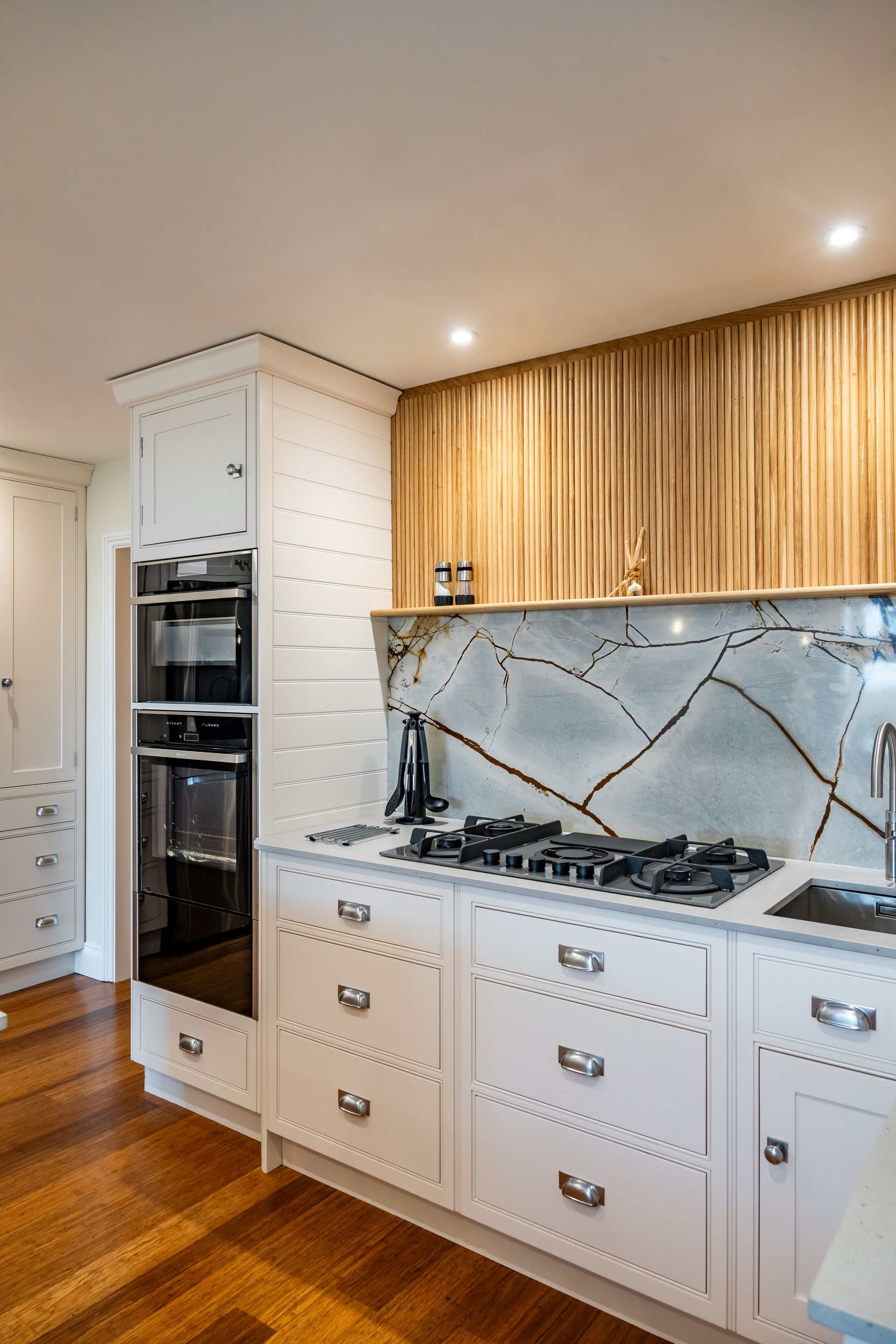 A kitchen with white cabinets and wooden floors and a stove top oven.