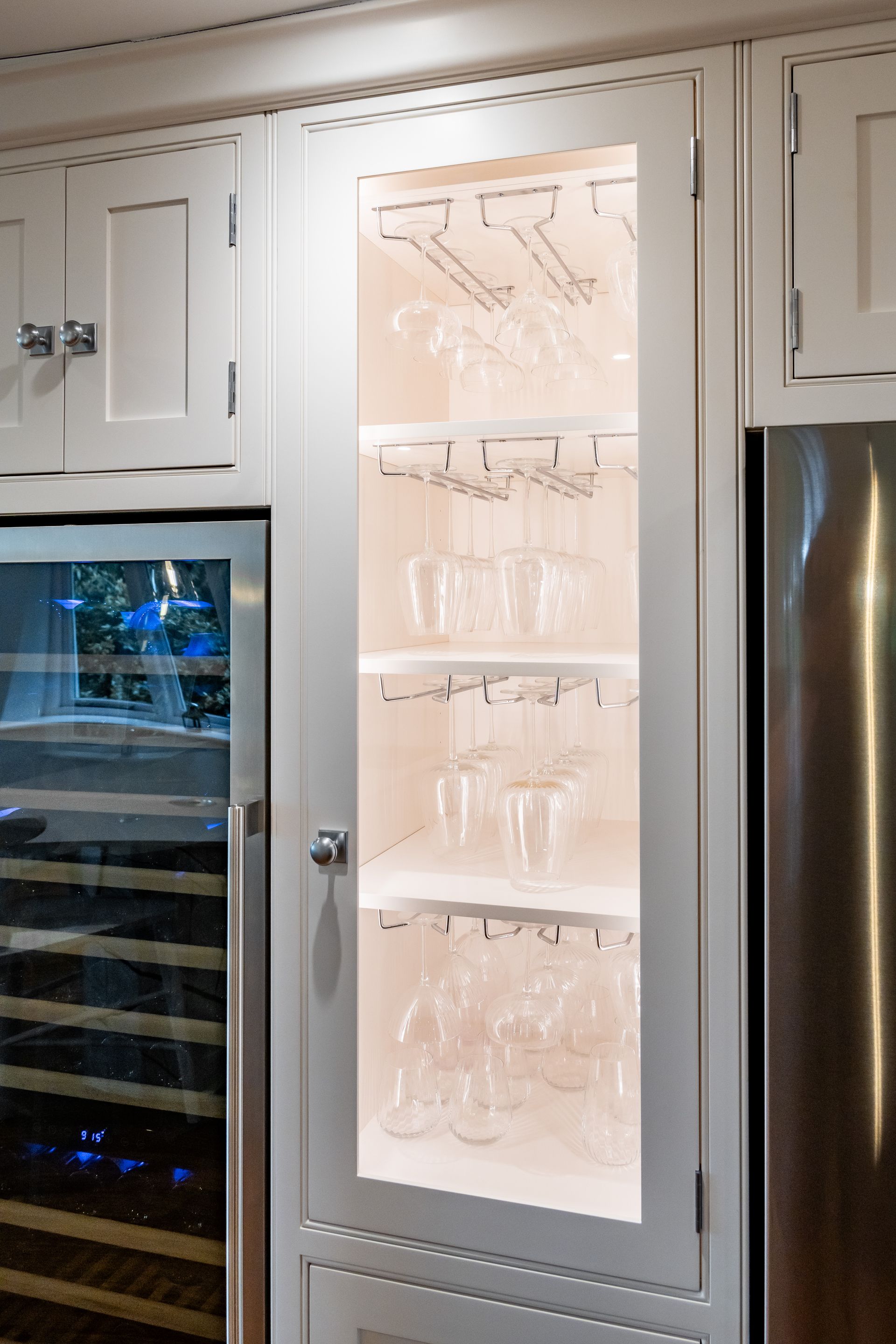 A wine cooler is behind a glass door with wine glasses on it.