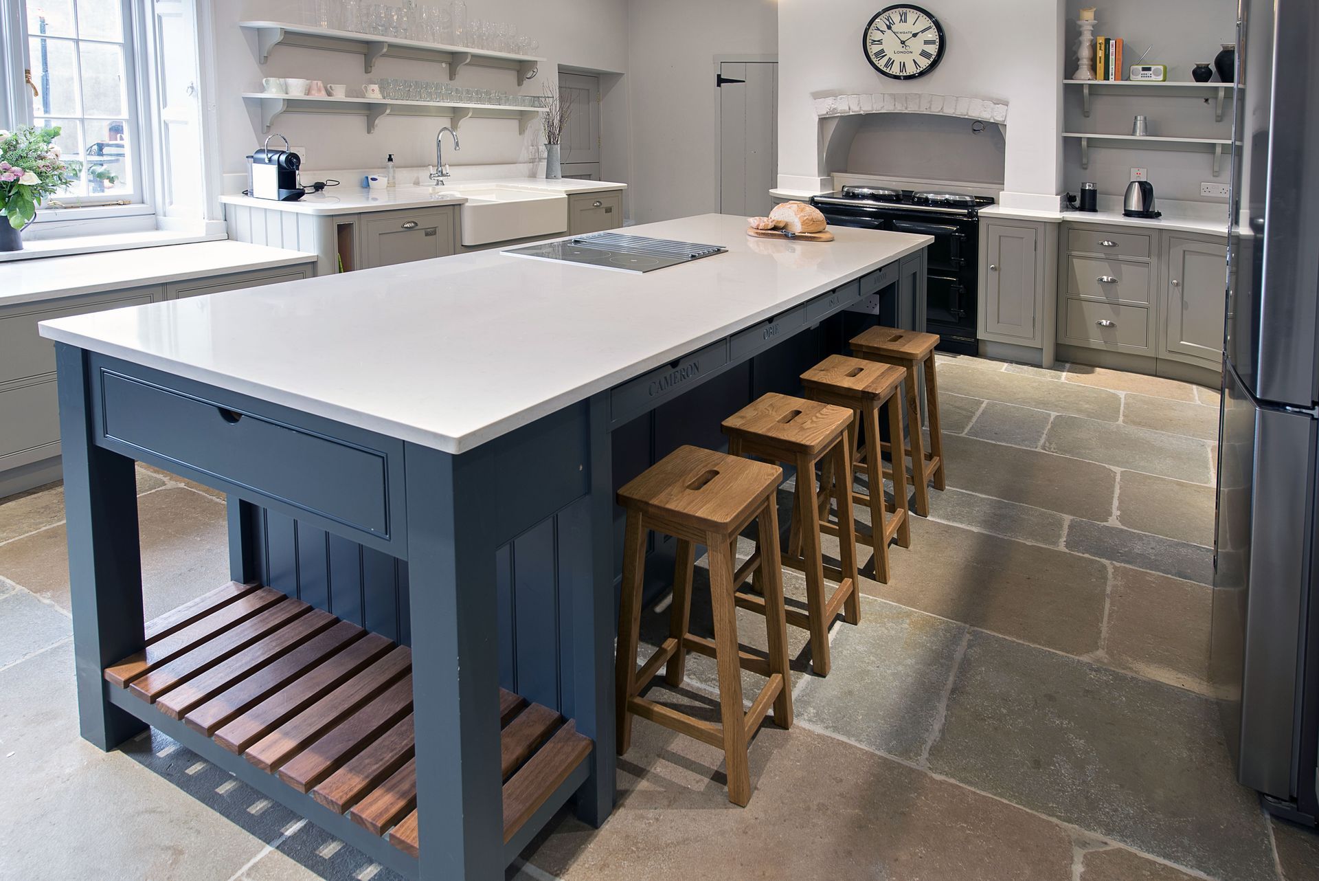 A kitchen with a large island and stools and a clock on the wall.